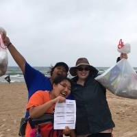 3 students showing the trash they have picked up and their tracking sheet